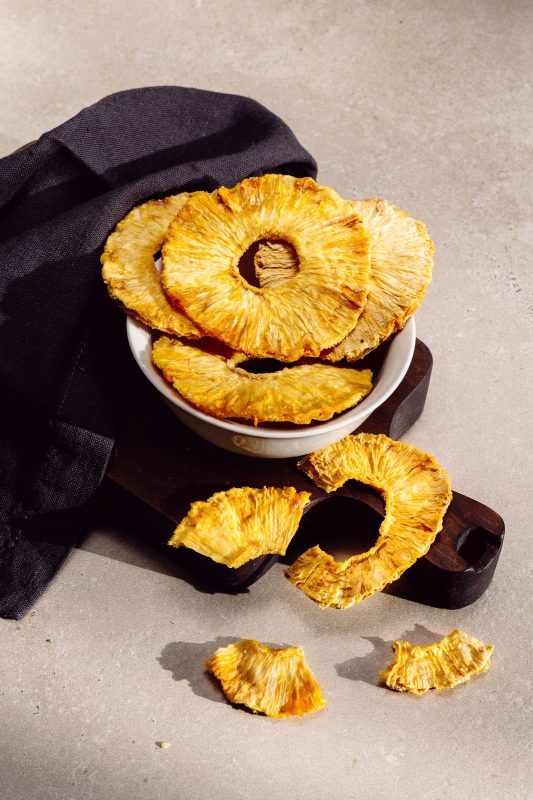 Golden dried pineapple rings in a white bowl on a dark wooden board