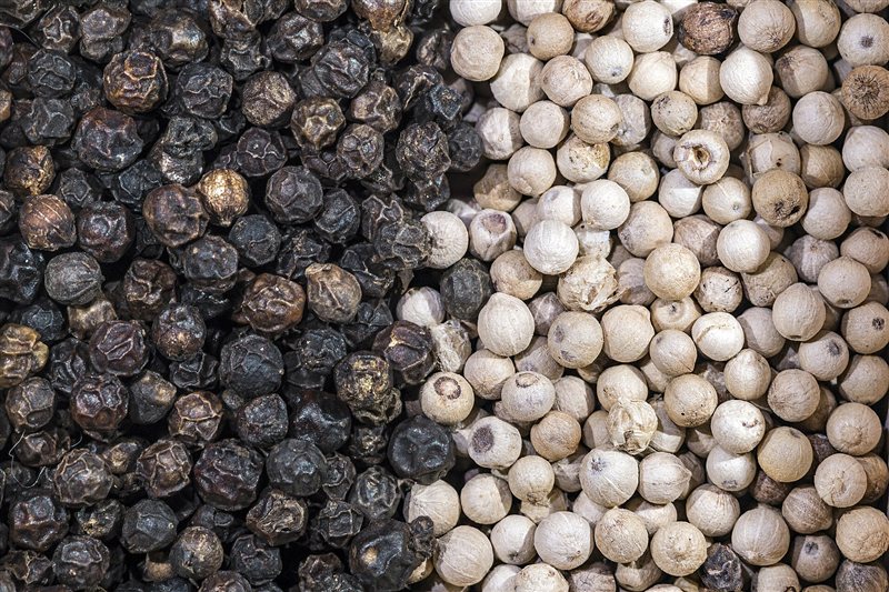 Black peppercorns with wrinkled dark skin beside smooth pale white peppercorns