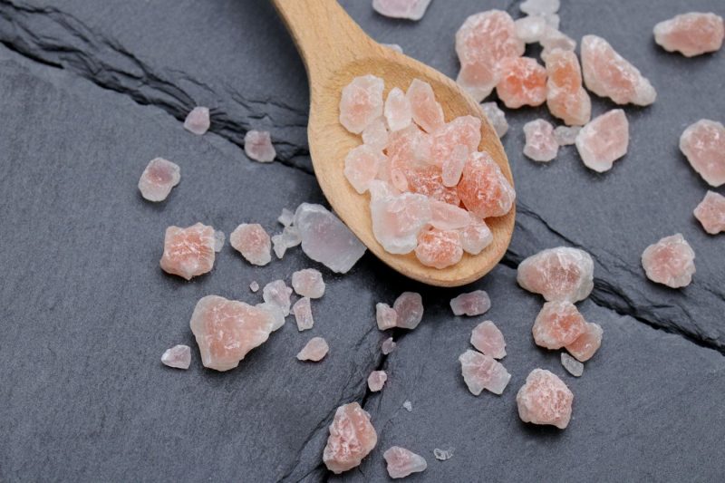 Pink Himalayan salt crystals on a wooden spoon and a slate surface