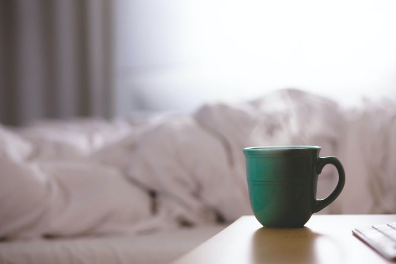 A mug of tea on a nightstand beside an unmade bed